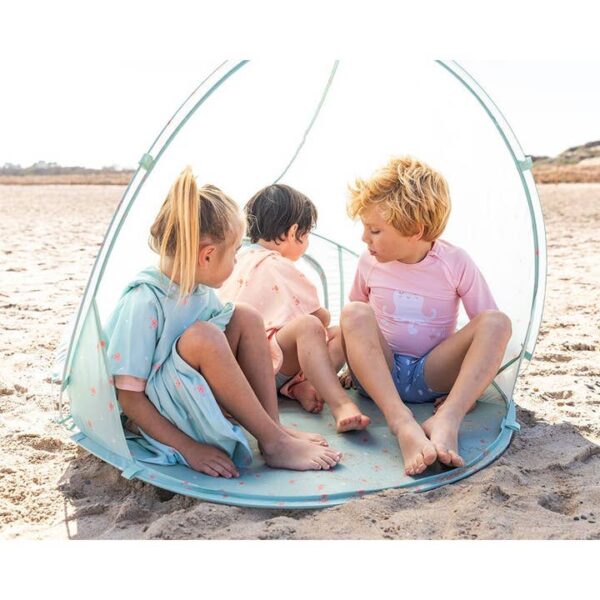 Drei Kinder spielen zusammen in einem Strandzelt am Strand.