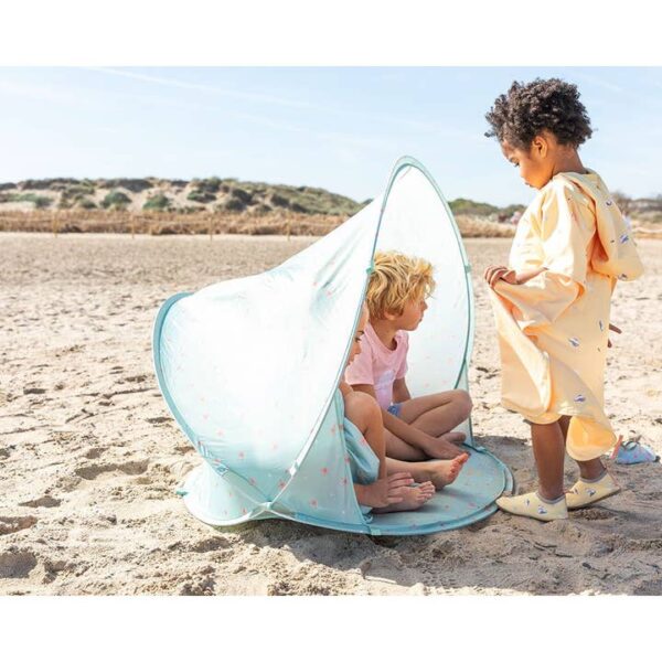 Zwei Kinder in einem Strandzelt am Strand, drittes Kind steht daneben.